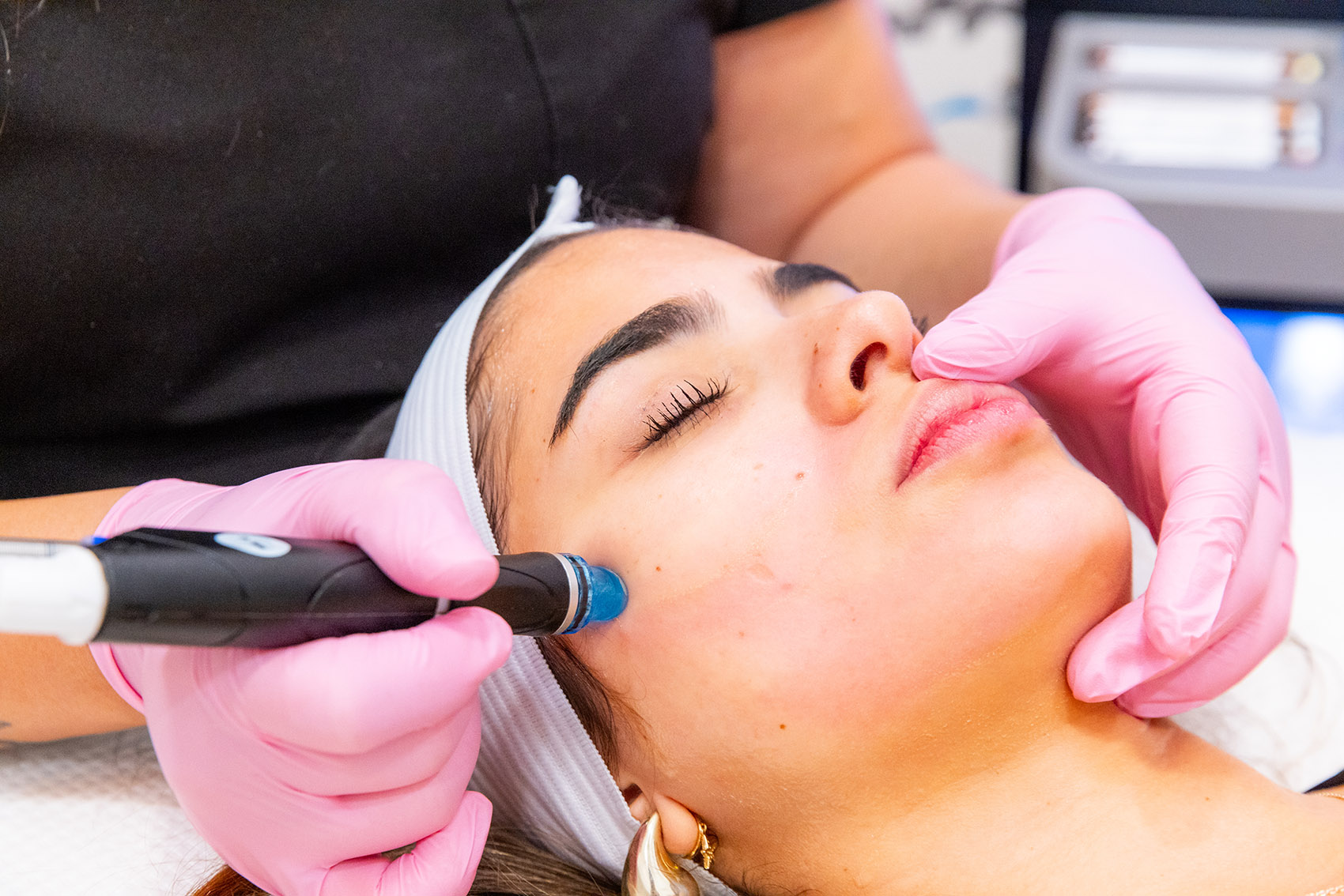 Close-up of a professional with pink gloves performing a HydraFacial in Toledo on a female patient