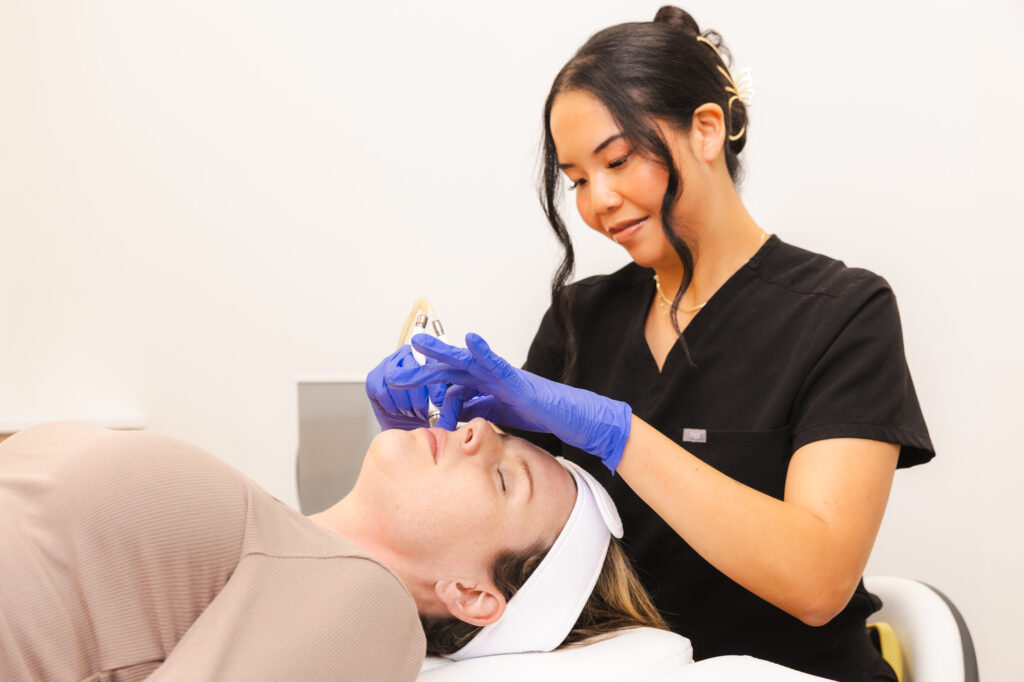 a provider wearing black scrubs and blue gloves performs microdermabrasion on a female patient's face to enhance her results from microneedling with radiofrequency in Perrysburg