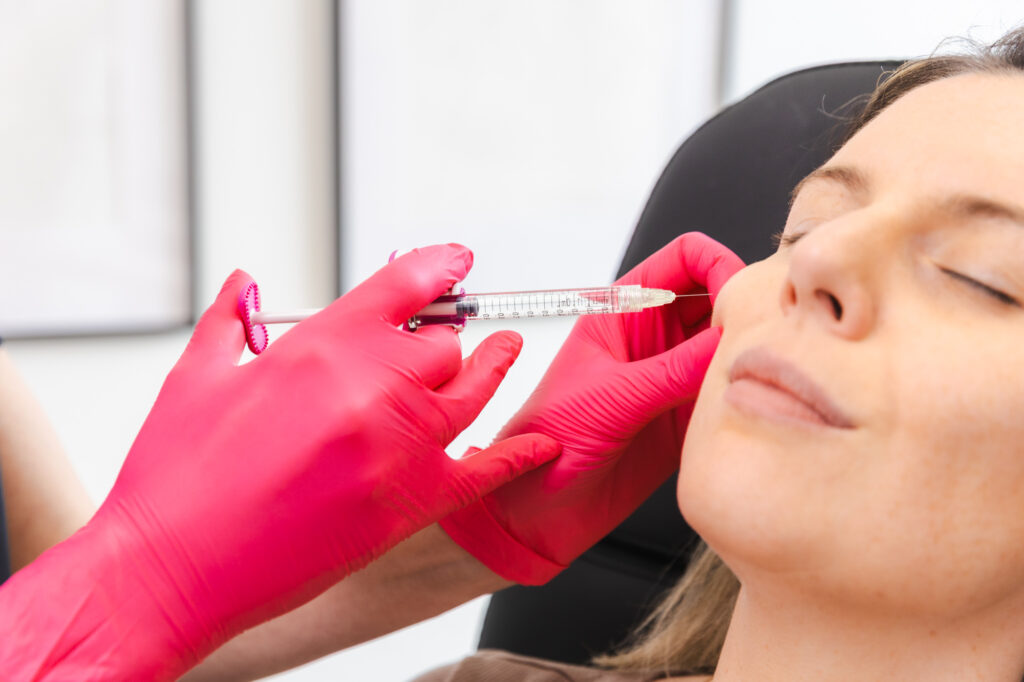 a provider wearing pink gloves performs collagen stimulating injections in Columbus, injecting a female patient's cheek